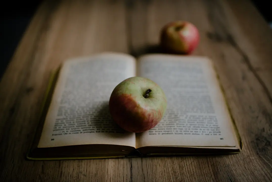Two apples and an open book on a wooden table, each outlined as a layer